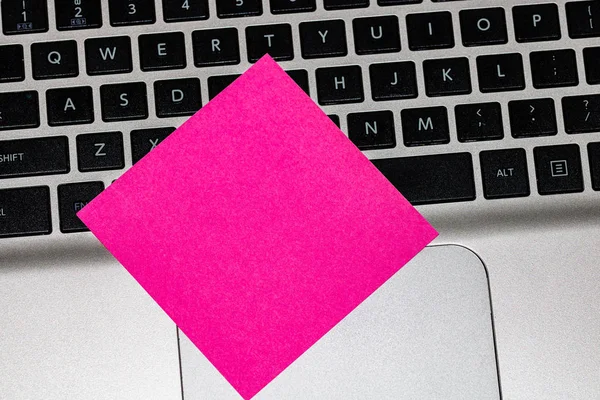 Blank pink sticky note, post it on keyboard. Close up.