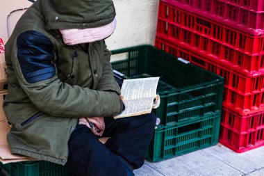 Homeless reading a book in front of a store in the winter, Bucha