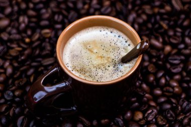 Kırmızı arka planda kavrulmuş kahve çekirdeği ve kahve fincanı.