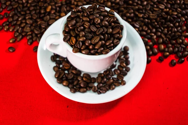 Кофейная чашка с жареными бобами на фоне красных и кофейных зерен — стоковое фото
