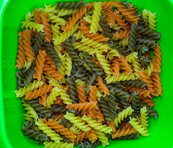 Composition of raw pasta uncooked tricolore fusilli, pasta twist shape. Close up and selective focus on colorful fusilli pasta. Fusilli pasta in bowl.