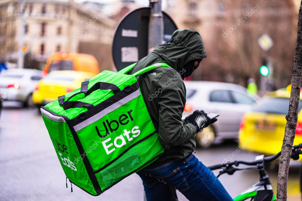 Young man on a bike with Uber Eats logo delivering food during a rainy day in Bucharest, Romania, 2020