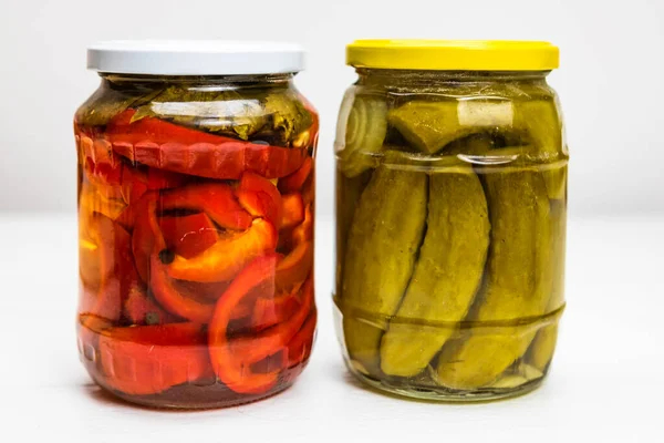 Glass jar with pickled red bell peppers and jar with pickled cucumbers (pickles) isolated.