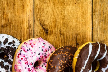 Ahşap masada renkli çörekler. Jöleli şekerli tatlı yiyecekler, çikolatalı donutlar. Kopyalama alanı olan üst görünüm