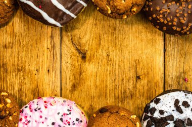 Ahşap masada renkli çörekler. Jöleli şekerli tatlı yiyecekler, çikolatalı donutlar. Kopyalama alanı olan üst görünüm