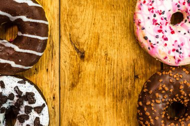 Ahşap masada renkli çörekler. Jöleli şekerli tatlı yiyecekler, çikolatalı donutlar. Kopyalama alanı olan üst görünüm