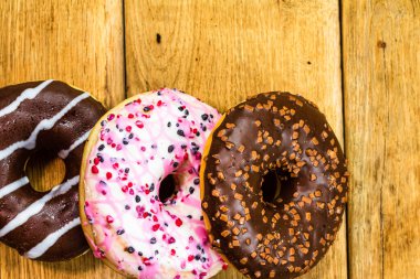 Ahşap masada renkli çörekler. Jöleli şekerli tatlı yiyecekler, çikolatalı donutlar. Kopyalama alanı olan üst görünüm