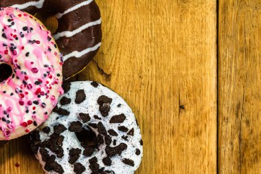 Ahşap masada renkli çörekler. Jöleli şekerli tatlı yiyecekler, çikolatalı donutlar. Kopyalama alanı olan üst görünüm