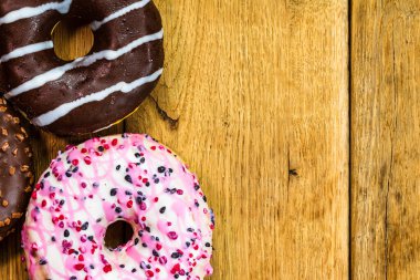 Ahşap masada renkli çörekler. Jöleli şekerli tatlı yiyecekler, çikolatalı donutlar. Kopyalama alanı olan üst görünüm