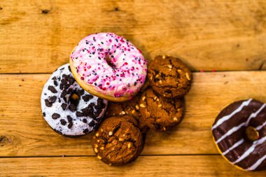 Ahşap masada renkli çörekler. Jöleli şekerli tatlı yiyecekler, çikolatalı donutlar. Kopyalama alanı olan üst görünüm