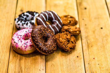 Ahşap masada renkli çörekler ve bisküviler. Jöleli şekerli tatlı yiyecekler, çikolatalı donutlar. Kopyalama alanı olan üst görünüm