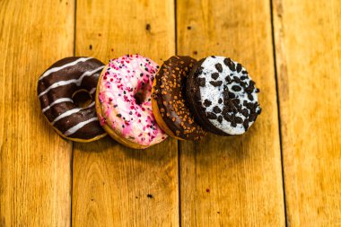 Ahşap masada renkli çörekler. Jöleli şekerli tatlı yiyecekler, çikolatalı donutlar. Kopyalama alanı olan üst görünüm