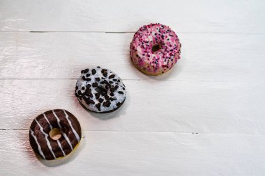 Beyaz ahşap masada renkli çörekler. Şekerli, şekerli, şekerli, şekerli, şekerli. Kopyalama alanı olan üst görünüm