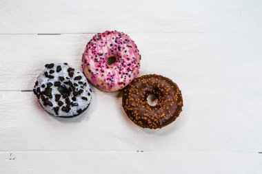 Beyaz ahşap masada renkli çörekler. Şekerli, şekerli, şekerli, şekerli, şekerli. Kopyalama alanı olan üst görünüm