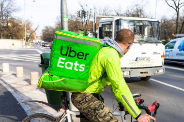 Uber Eats logosuna sahip bisikletli genç adam, 2020 Bükreş, Romanya 'da yiyecek dağıtıyor.