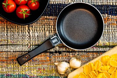 Küçük tava, sarımsak, makarna ve kırsal bir peçetede taze vişneli domates manzarası. Malzemeler ve gıda konsepti