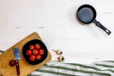 Bıçak manzarası, küçük tava, soğan, sarımsak ve taze vişneli domatesler kırsal beyaz ahşap bir masada küçük siyah kasede. Malzemeler ve gıda konsepti
