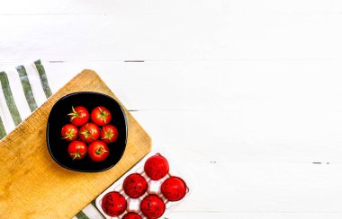 Taze kiraz domatesleri ve kırsal beyaz ahşap bir masada kırmızı paskalya yumurtaları. Malzemeler ve gıda konsepti