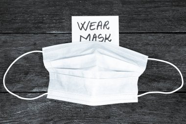 Hatırlatma notuna maske takmak ve tahta masaya cerrahi maske takmak. Avrupa 'da yayılan grip virüsü, virüs koruma yöntemleri konsepti.