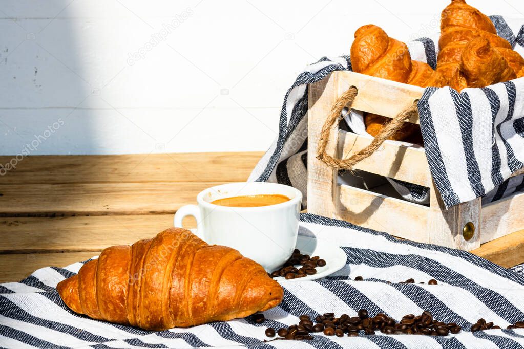 Puff pastry, coffee cup and buttered French croissant on wooden crate. Food and breakfast concept. Detail of coffee desserts and fresh pastries