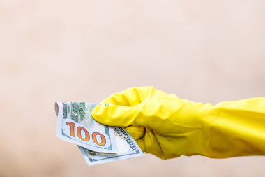 Dünya para kavramı, eldiven alma, 100 dolarlık banknot verme ya da tutma, bulanık arka planda izole edilmiş. Corona virüsü COVID-19 salgını. Virüsün yayılmasını önleme kavramı