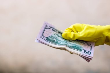 Dünya para kavramı, eldiven alma, 50 dolarlık banknot verme ya da tutma, bulanık arka planda izole edilmiş. Corona virüsü COVID-19 salgını. Virüsün yayılmasını önleme kavramı