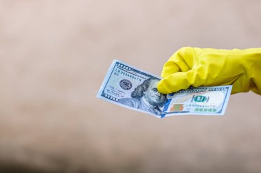 Dünya para kavramı, eldiven alma, 100 dolarlık banknot verme ya da tutma, bulanık arka planda izole edilmiş. Corona virüsü COVID-19 salgını. Virüsün yayılmasını önleme kavramı