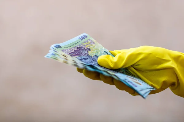 World money concept, hand with gloves receiving, giving or holding 100 LEI banknote, Romanian currency isolated on blurred background. COVID-19 outbreak. Concept of prevention virus spread