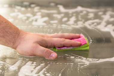 Sünger ve temizlik spreyi kullanarak cam masayı temizleyen adam, temizlik hizmeti konsepti. Ev işleri ve ev idaresi kavramı