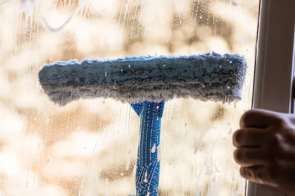 Man cleaning window using window cleaning squeegee and cleaning sprayer, cleaning services concept. Housework and housekeeping concept