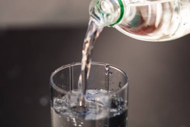 Plastik şişeden bulanık arka plandaki bir bardağa su dökülüyor. Seçici odak ve kopyalama alanı