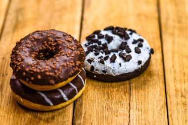 Ahşap masada renkli çörekler. Jöleli şekerli tatlı yiyecekler, çikolatalı donutlar. Kopyalama alanı olan üst görünüm