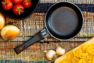 Küçük tava, soğan, sarımsak, makarna ve kırsal bir peçetede taze vişneli domates manzarası. Malzemeler ve gıda konsepti