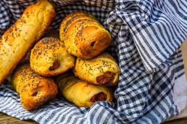 Hamurda pişmiş sosisler tuzlu ve haşhaş tohumlarıyla dolu kırsal bir sepetin içinde. Sosisli börekler, ev yapımı lezzetli hamur işleri..