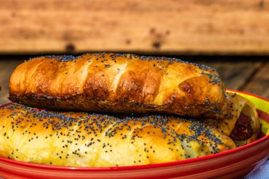 Hamurda pişmiş sosisler tuzlu ve haşhaş tohumları serpiştirilmiş, kırsal bir kompozisyonda. Sosisli börek, lezzetli ev yapımı hamur işleri..