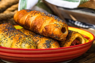 Hamurda pişmiş sosisler tuzlu ve haşhaş tohumları serpiştirilmiş, kırsal bir kompozisyonda. Sosisli börek, lezzetli ev yapımı hamur işleri..
