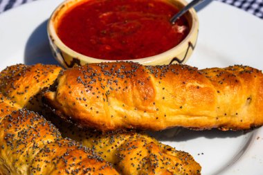 Hamur, tuz ve haşhaş tohumları serpiştirilmiş sosisler ve kırsal bir kompozisyonda domates sosu serpiştirilmiş kaseler. Sosisli börek, lezzetli ev yapımı hamur işleri..