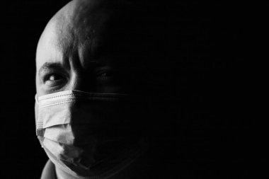 Pandemik ev izolasyonu, tıbbi koruyucu yüz maskesi olan adam siyah üzerine izole edilmiş.