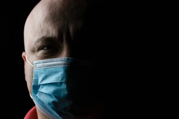 Pandemic home isolation, man with medical protective face mask isolated on black with copy space