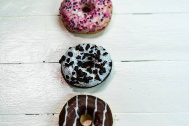 Beyaz ahşap masada renkli çörekler. Şekerli, şekerli, şekerli, şekerli, şekerli. Kopyalama alanı olan üst görünüm