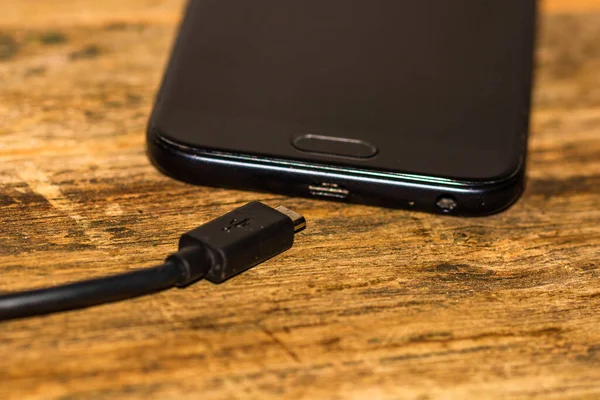 Close-up of black smartphone charging battery with an USB cable on wooden table with copy space .