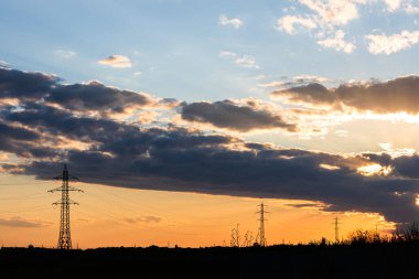 Güzel dramatik gökyüzü ve bulutlar, gün batımının ışıkları iletim kulesinin üzerinde (elektrik direği) bir tarlada.