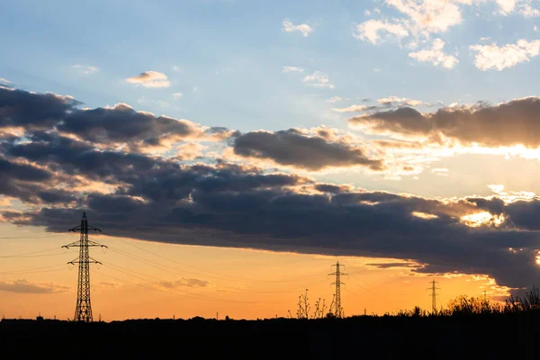 Güzel dramatik gökyüzü ve bulutlar, gün batımının ışıkları iletim kulesinin üzerinde (elektrik direği) bir tarlada.