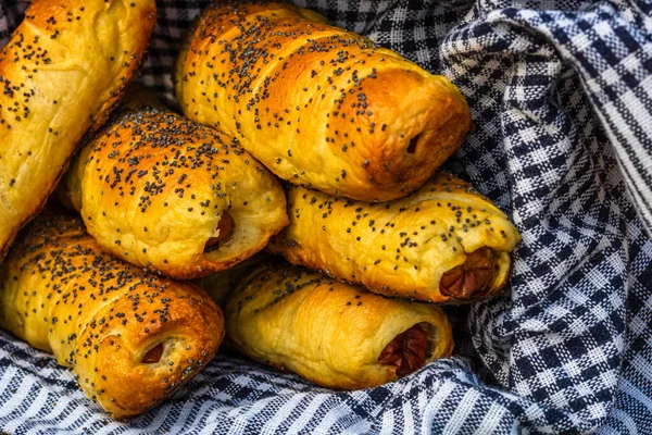 Hamurda pişmiş sosisler tuzlu ve haşhaş tohumlarıyla dolu kırsal bir sepetin içinde. Sosisli börekler, ev yapımı lezzetli hamur işleri..