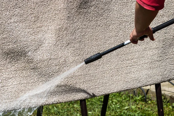 Close up of washing carpets with high pressure washer. Cleaning the carpet with a gun for washing high pressure water. House cleaning concept.