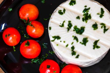 Kahvaltı, peynir ve kiraz domatesleri tabakta, ahşap ahşap tahta bir masa arkasında..