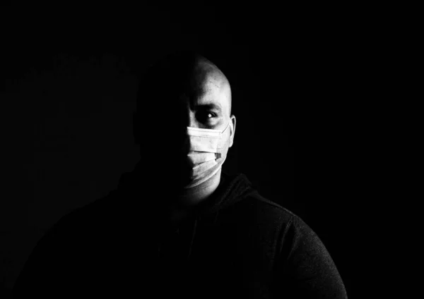 BW photo of sick young man with medical protective face mask illustrates pandemic coronavirus, Covid 19 disease isolated on black. Covid-19 outbreak, flu contamination and healthcare concept