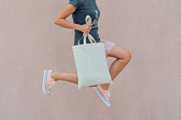 Woman in pink shorts and sneackers is jumping with white cotton bag in her hands. — Stock Photo, Image