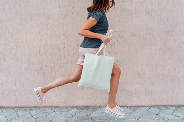 Mujer en pantalones cortos y zapatillas de deporte de color rosa está saltando con un bolso de algodón blanco en sus manos . — Foto de Stock