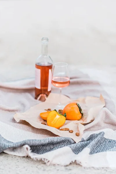 Picknick am Strand mit Kaki, Mandeln und einer Flasche Rosenwein auf beiger Decke. — Stockfoto